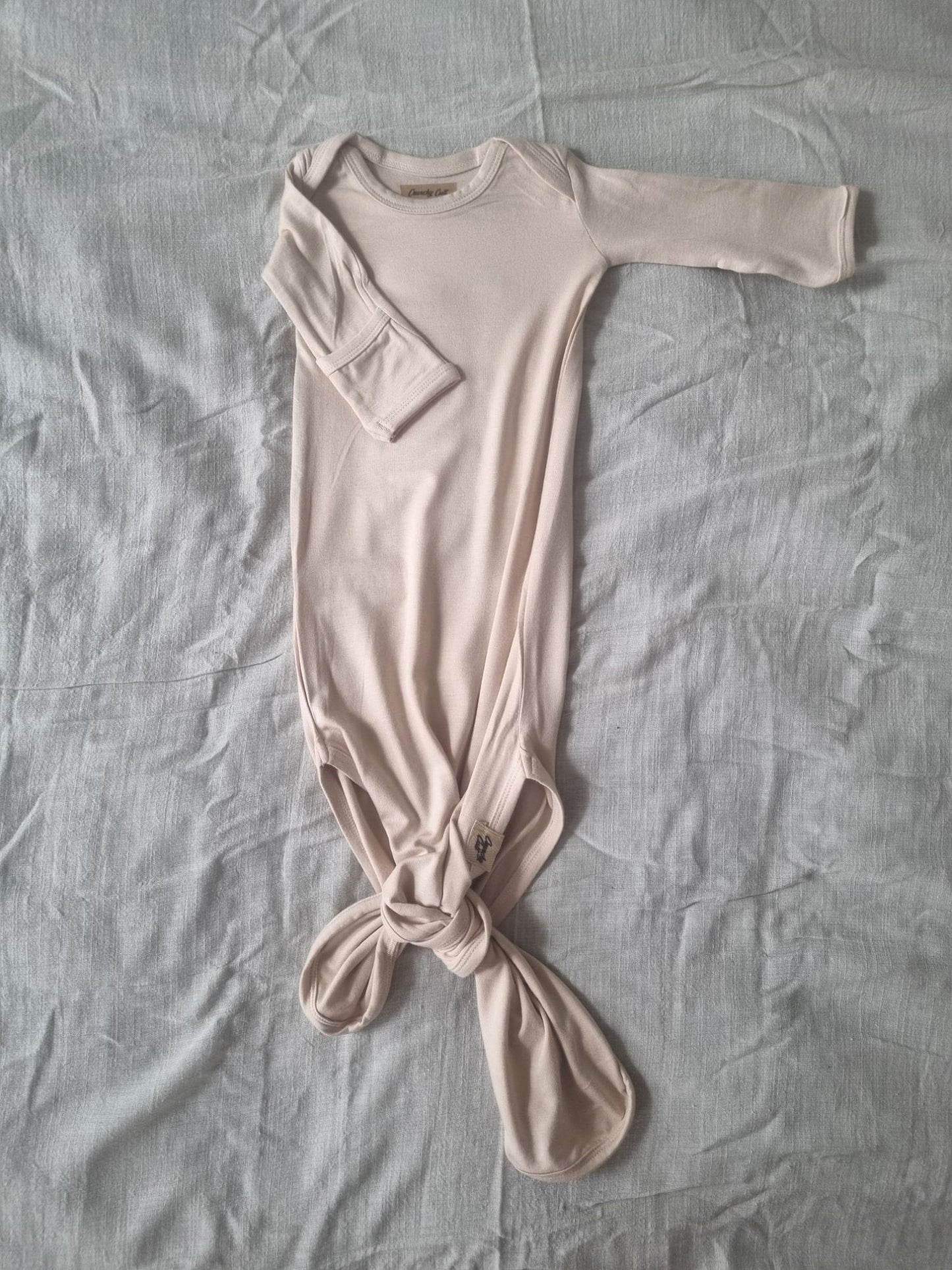 Baige knotted baby gown on a grey linen sheet, front view