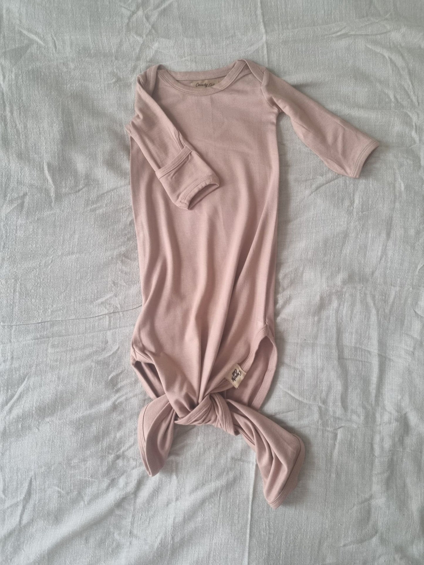 Brown knotted baby gown on a grey linen sheet, front view
