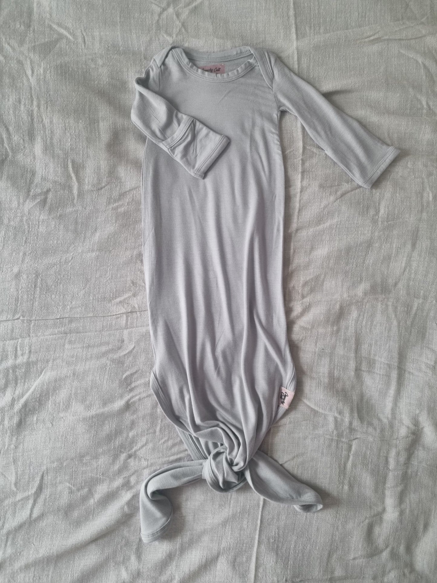 Grey knotted baby gown on a grey linen sheet, front view