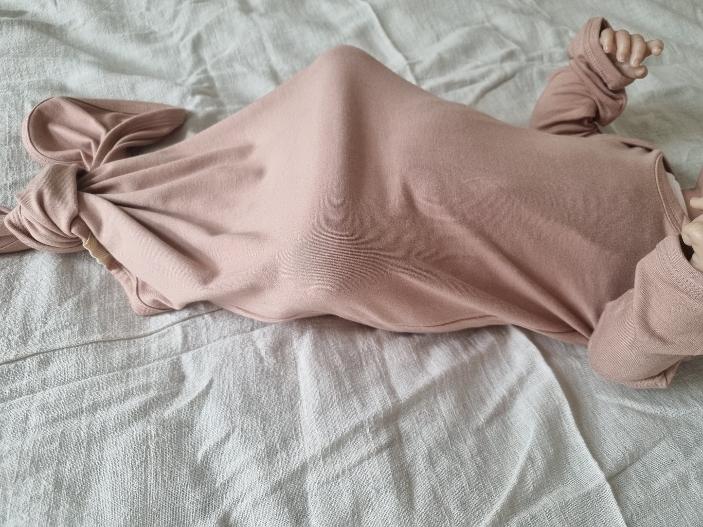 Brown knotted baby gown modeled by baby, side view, laying on grey linen sheet