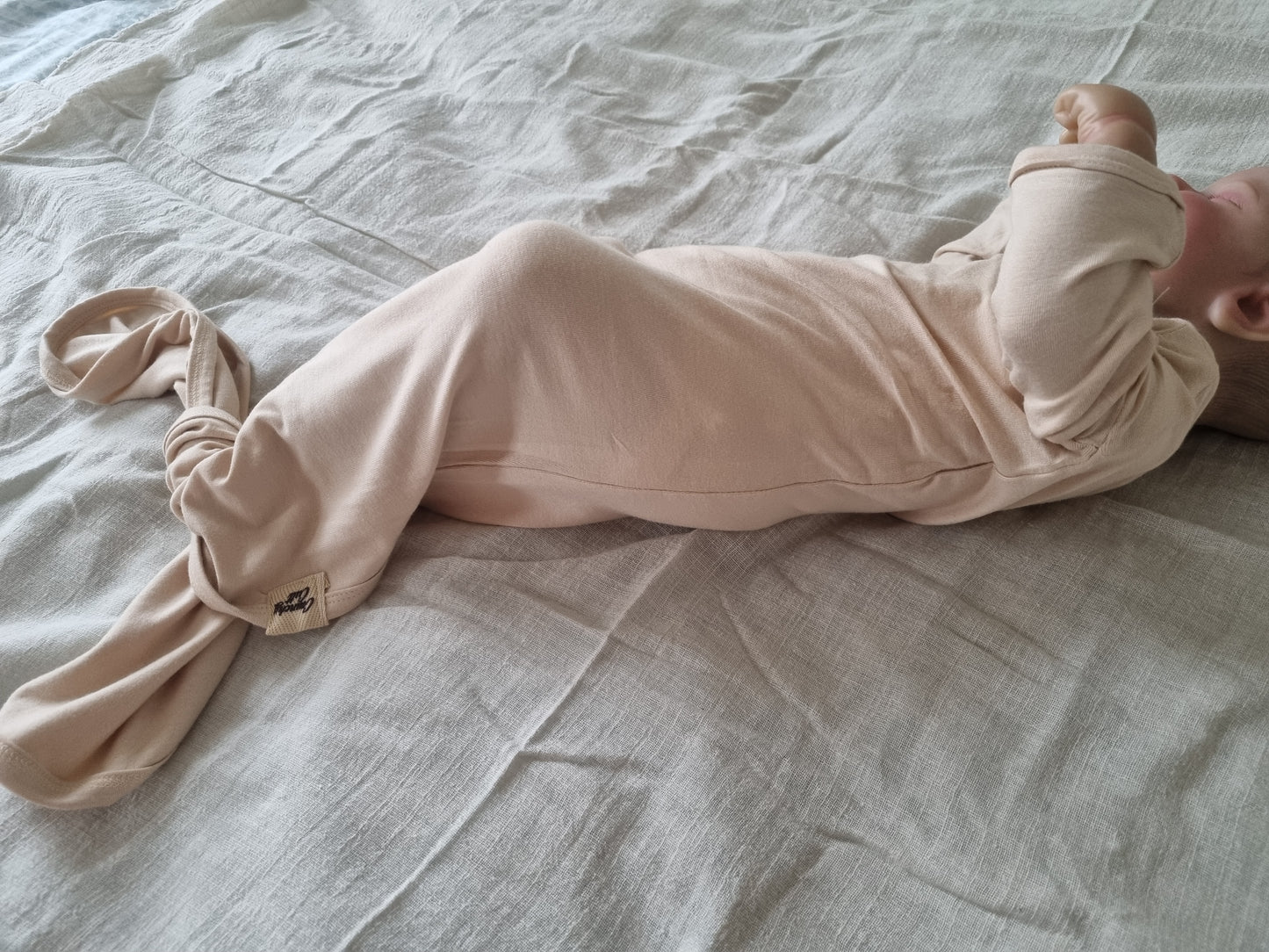 Baby modeling baige baby gown on grey linen sheet, side view