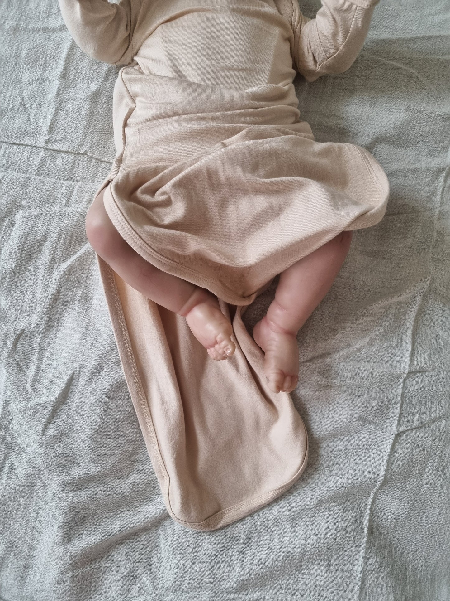 Baige gown modeled by baby with the bottom open and feed out. Baby laying down on grey linen sheet
