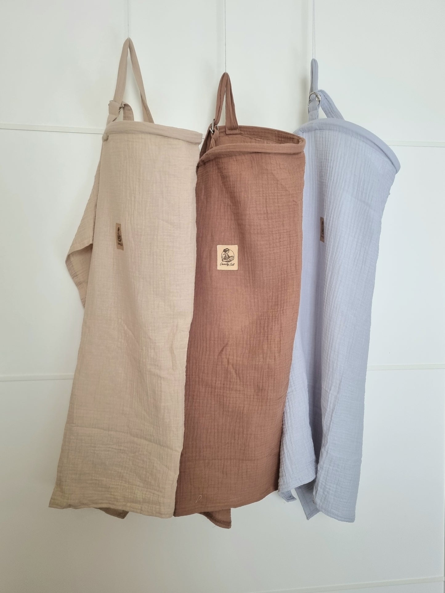 Set of three breastfeeding covers hanging. baige, brown, and grey covers. Front view