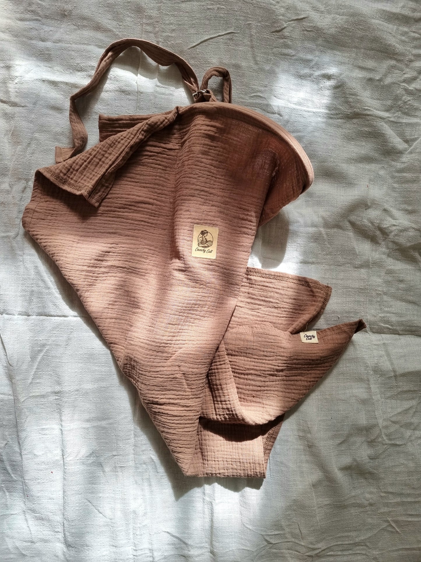 Brown breastfeeding cover, crunched up on table with linen sheet. Top view