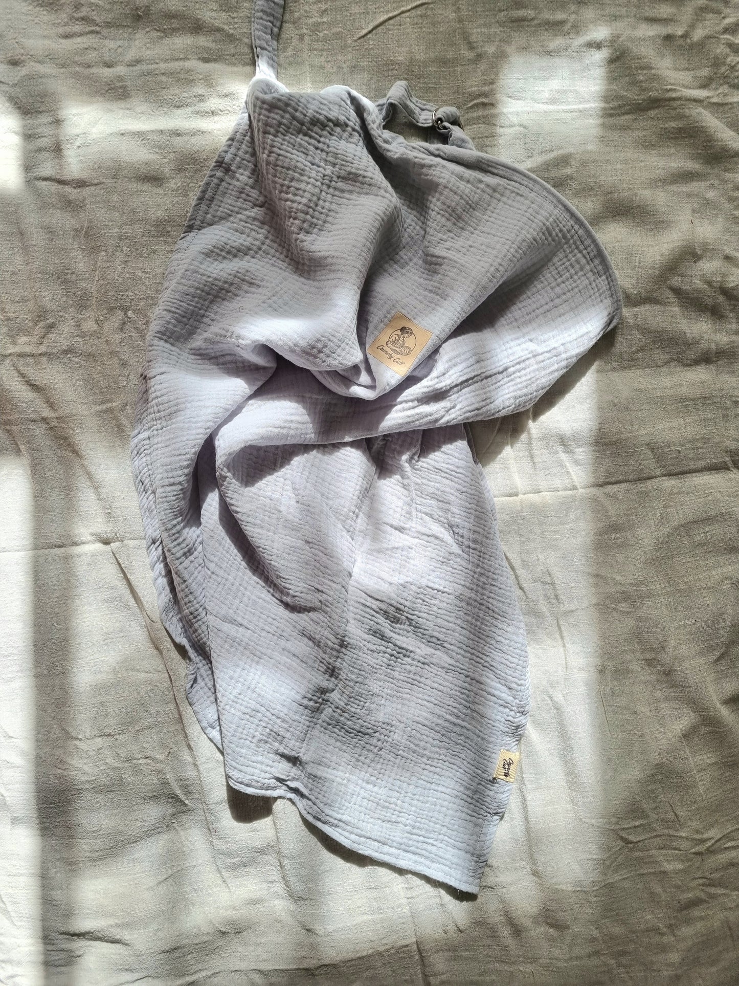 Grey breastfeeding cover, crunched up on table with linen sheet. Top view