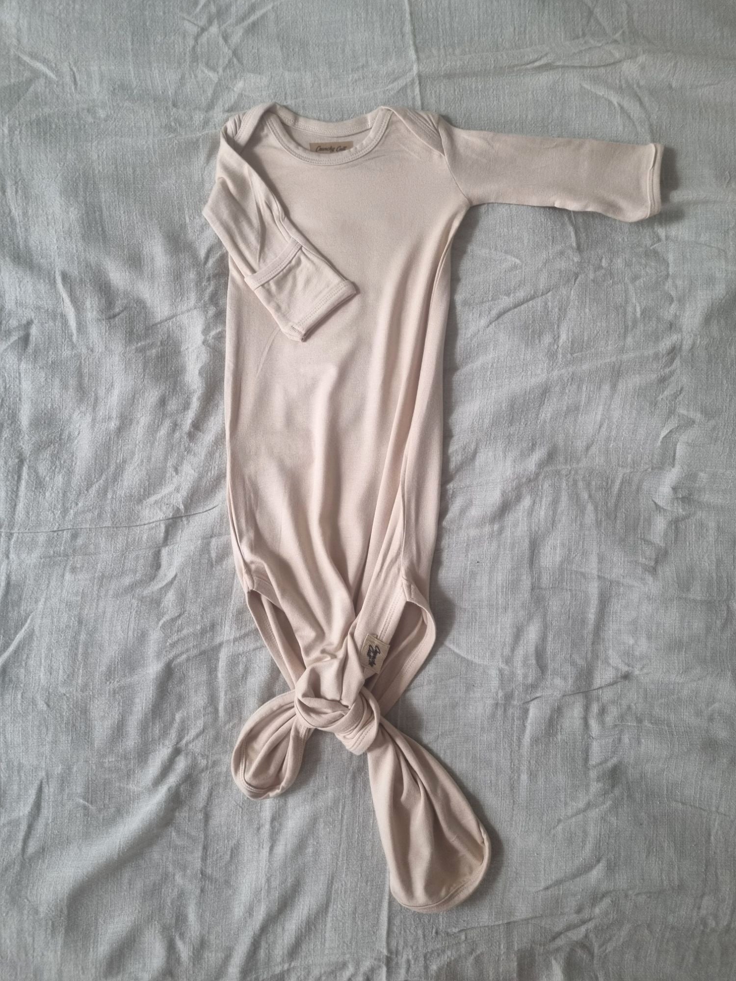 Baige knotted baby gown on a grey linen sheet, front view