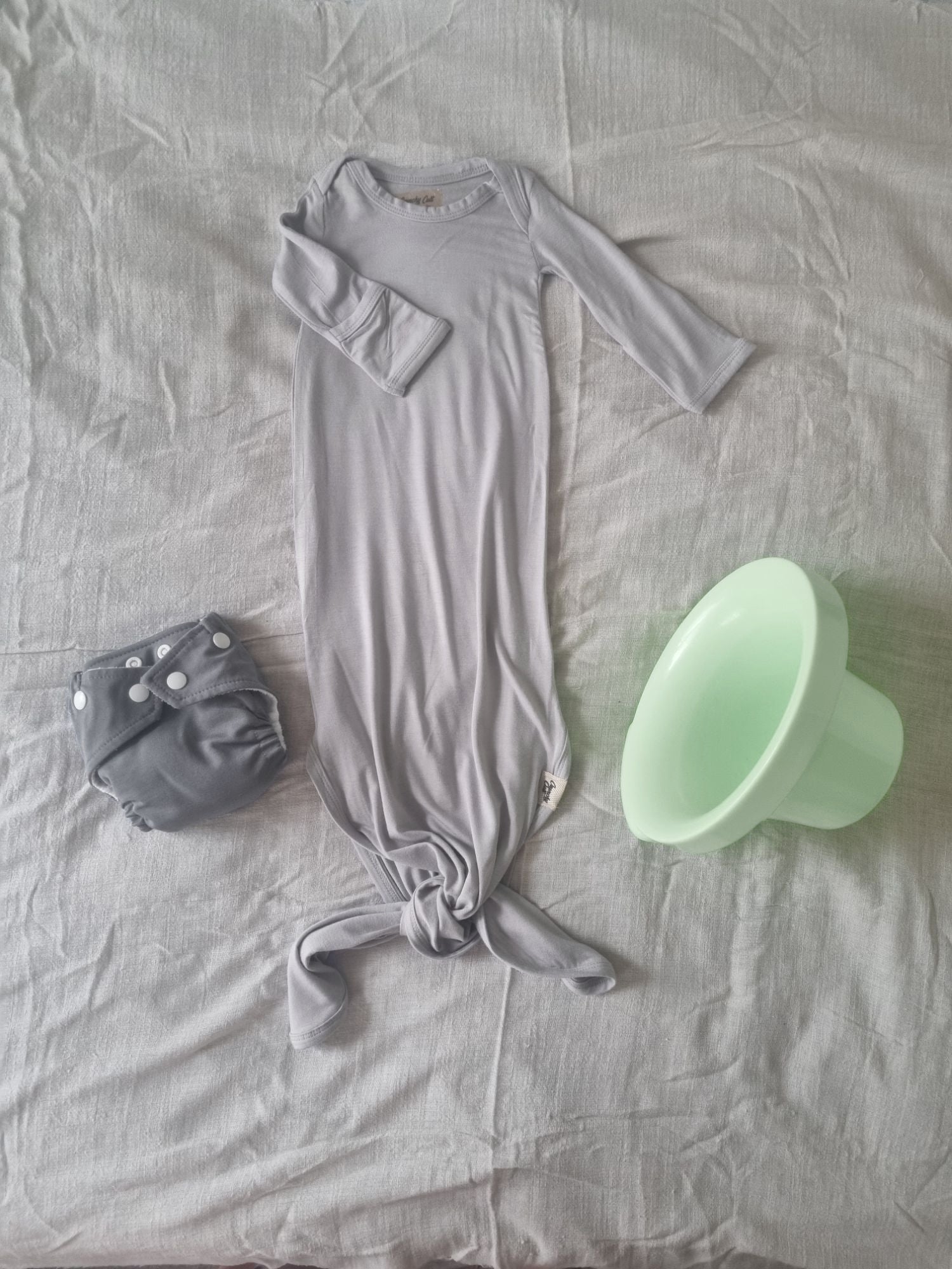 Grey knotted baby gown, front view, rolled rolled sleve, decorated background with grey linen sheet and top hat potty and grey cloth nappy.