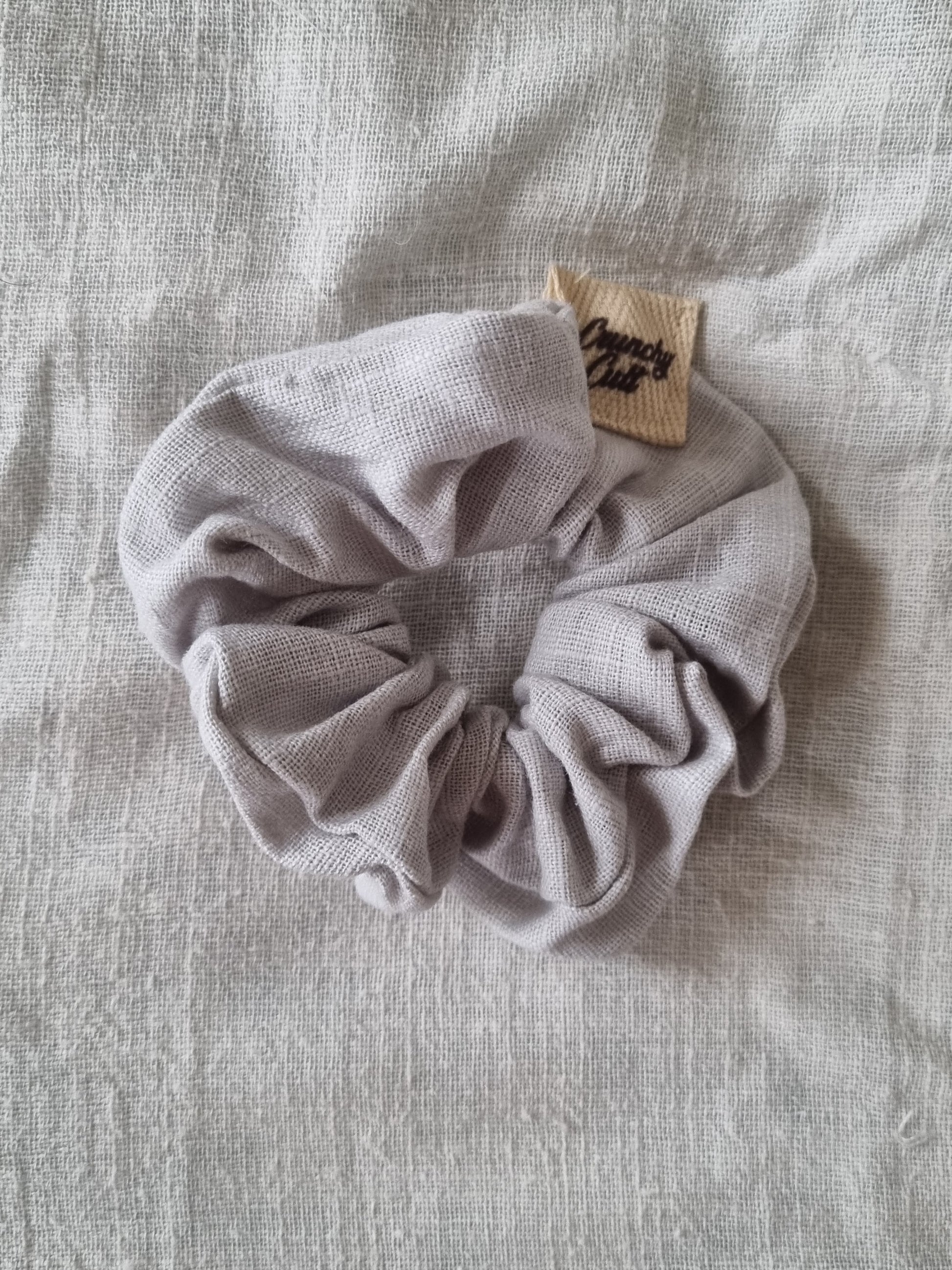 Grey linen hair scrunchy, single, top view, modelled on grey sheet