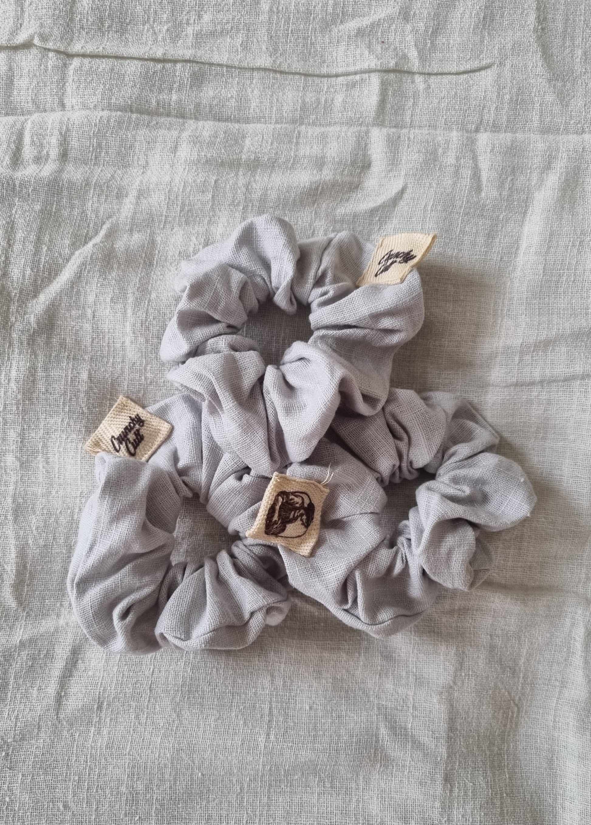 Three linen grey hair scrunches modelled on a grey linen sheet