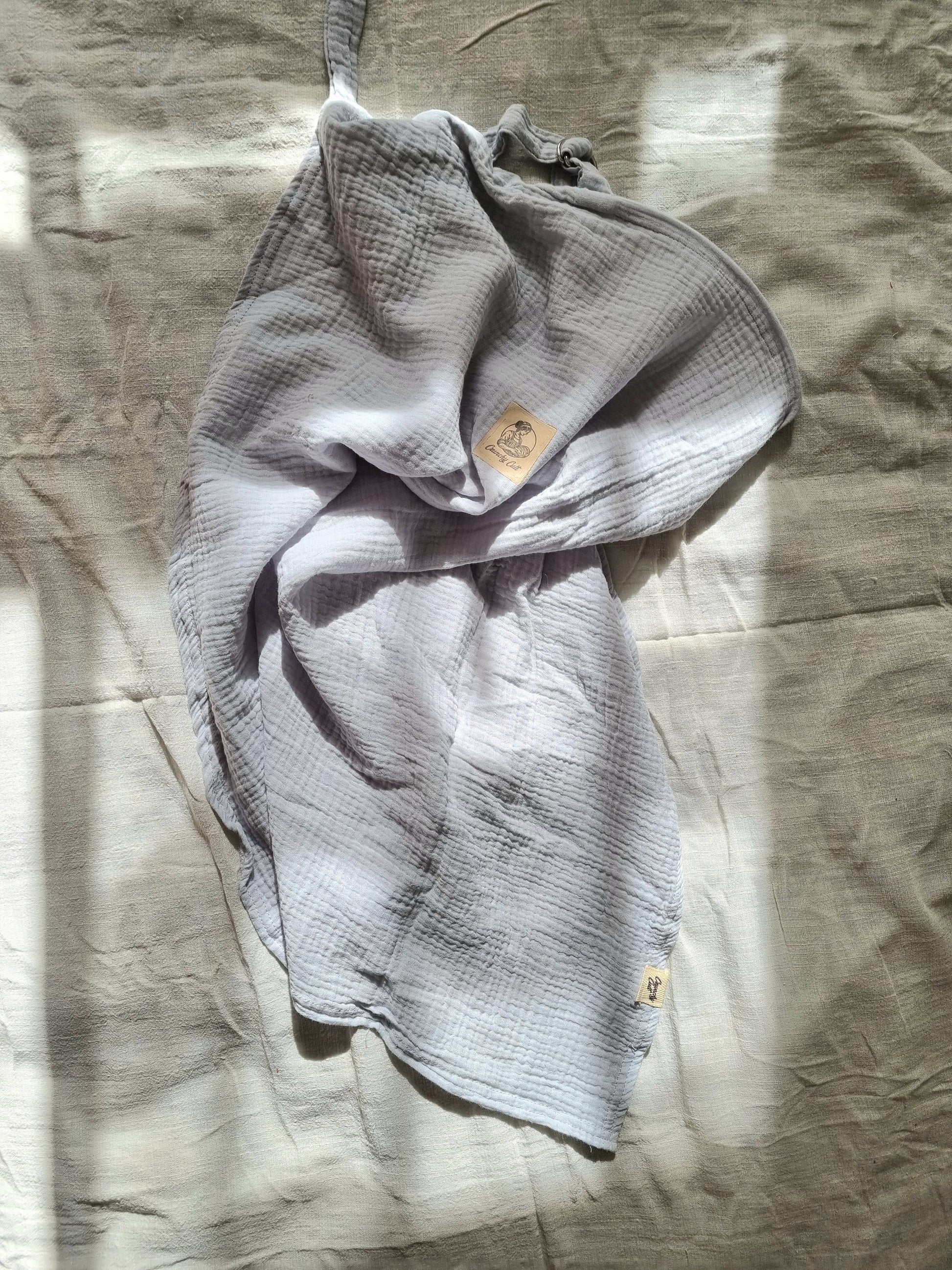 Grey breastfeeding cover, crunched up on table with linen sheet. Top view