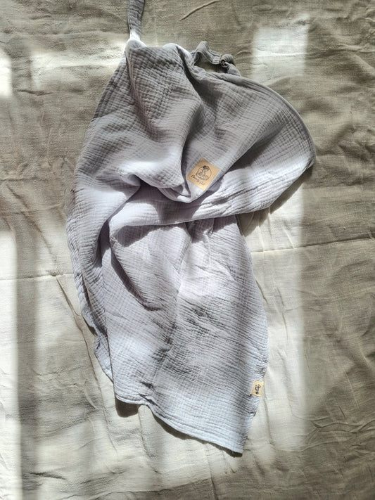 Grey breastfeeding cover, crunched up on table with linen sheet. Top view